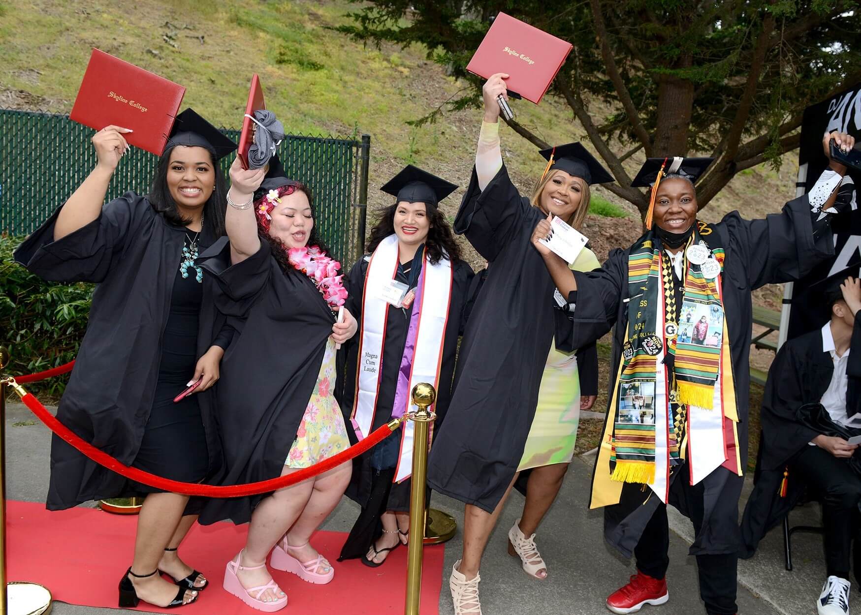 a group of graduates celebrate with their diplomas, backstage at Commencement