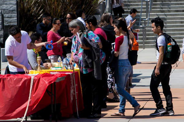 a line of students approach a group of students at a table in the quad