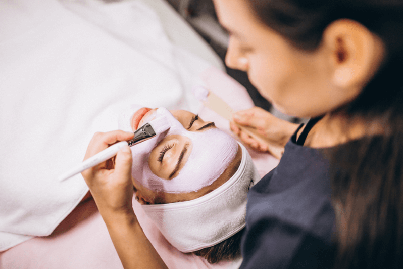 woman brushes a facial mask onto a client's face