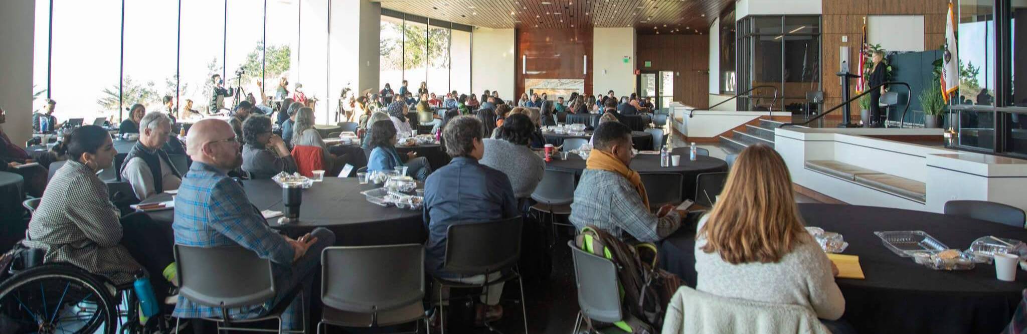 group of professionals seated at tables in a large room listen to a speaker at a Flex Day event