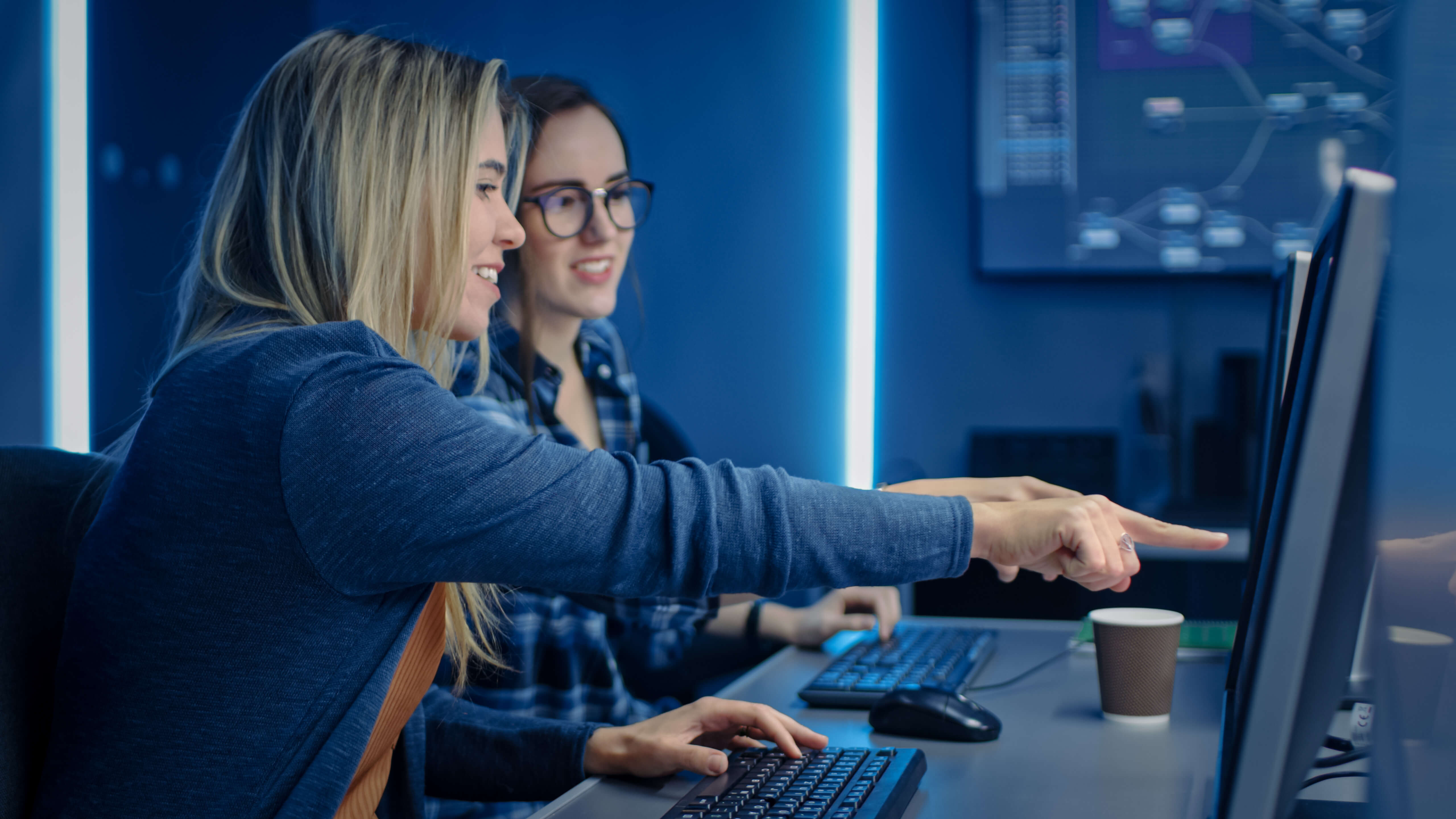 two smiling women review a computer screen together, one points at something onscreen