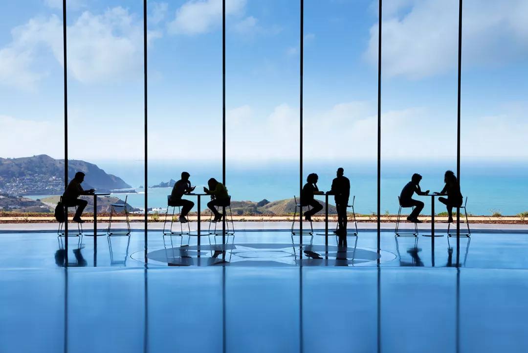 silhouetted students sitting at tables in front of ocean view