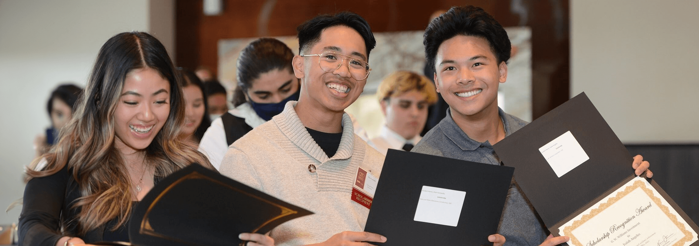 three students at a scholarship awards ceremony holding their awards and smiling