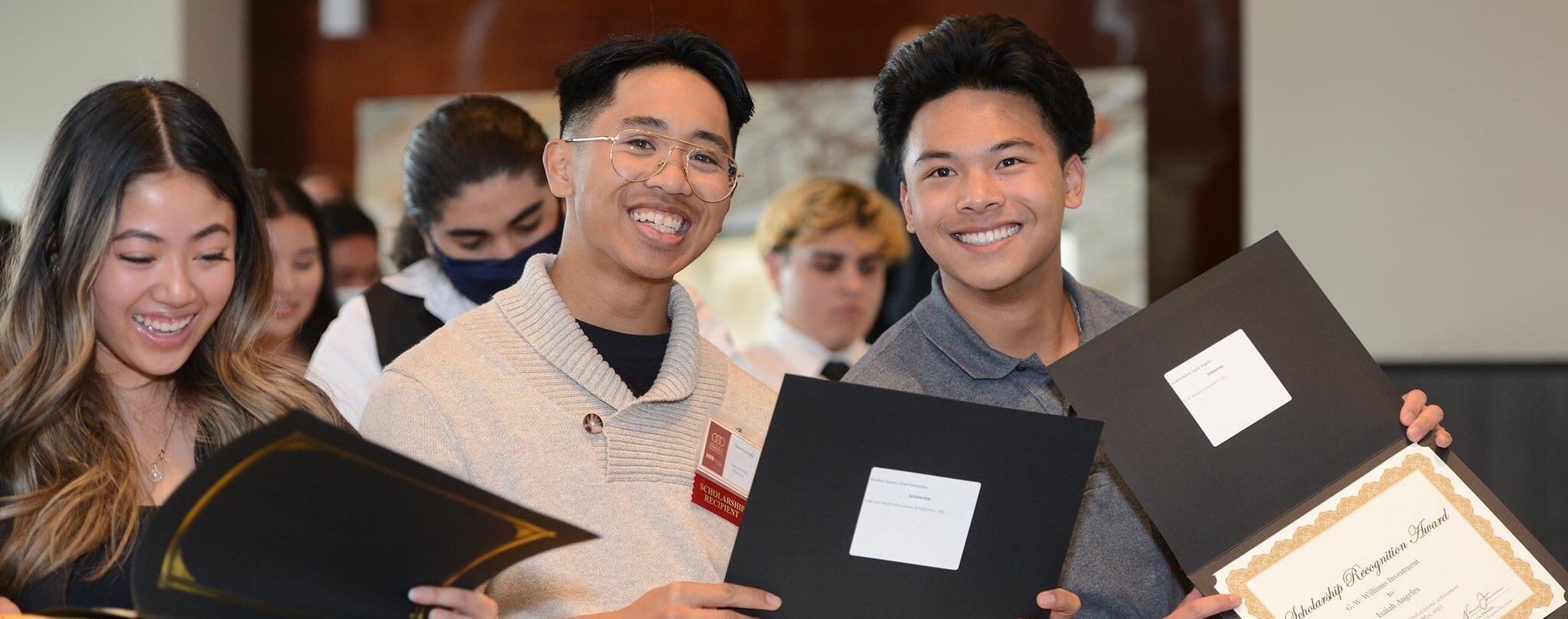 three students at a scholarship awards ceremony holding their awards and smiling