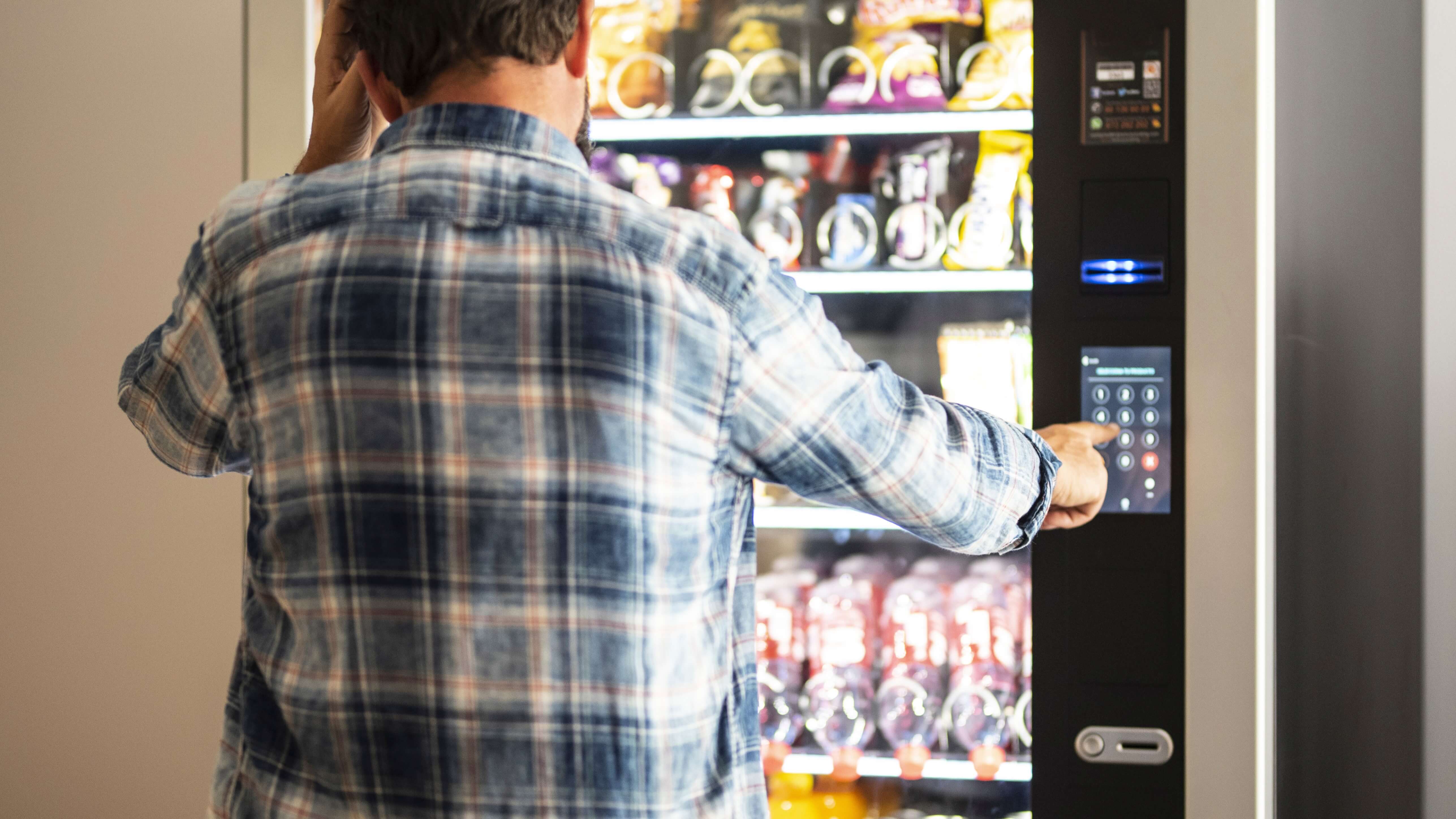 man in a plaid shirt operates a vending machine full of snacks