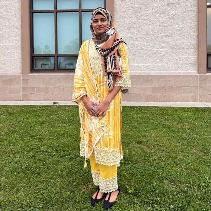 Ifra Khanam poses on a lawn in a yellow salwar kameez and colorful headscarf