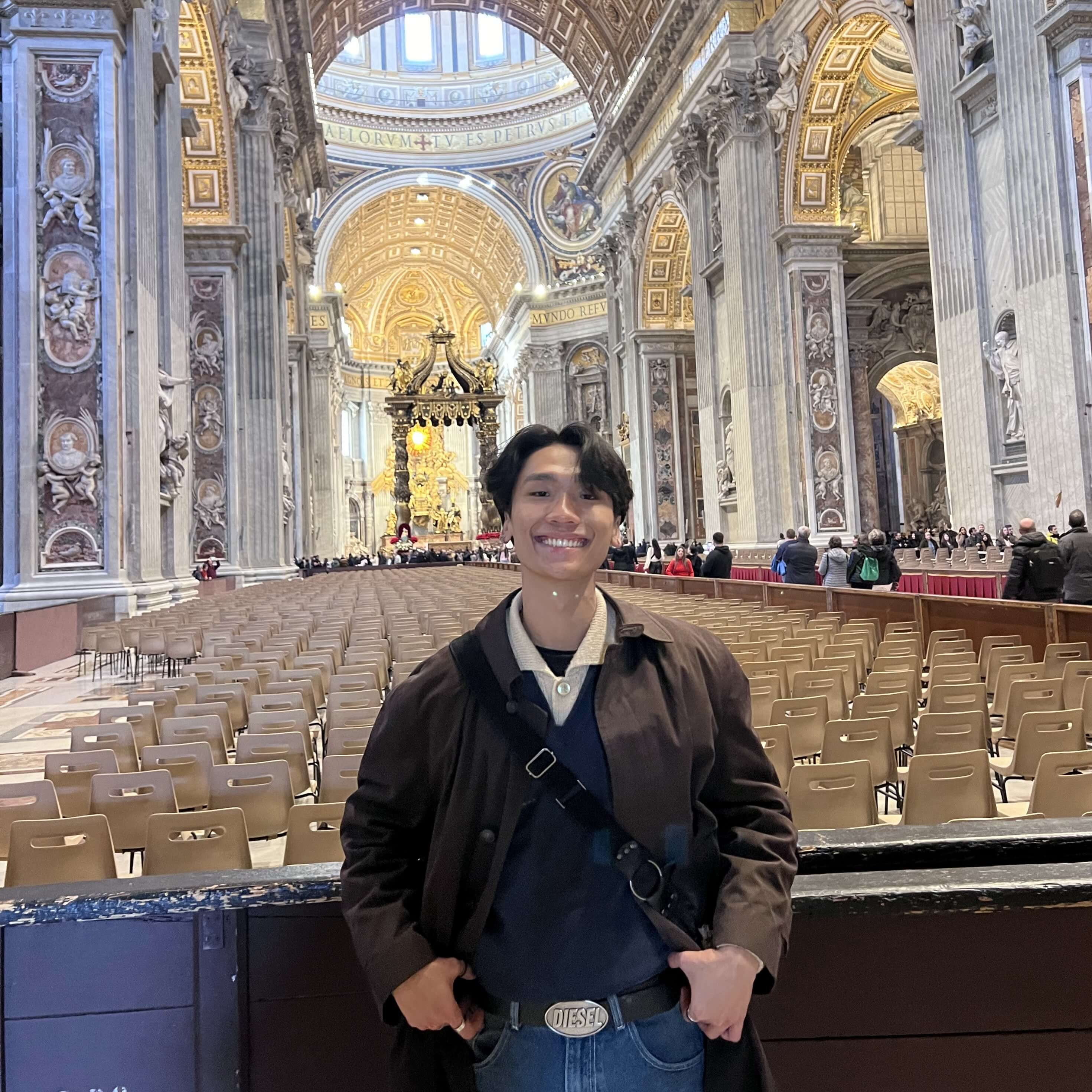 Nien Ngo smiles, standing in front of a pew inside a grandly decorated cathedral