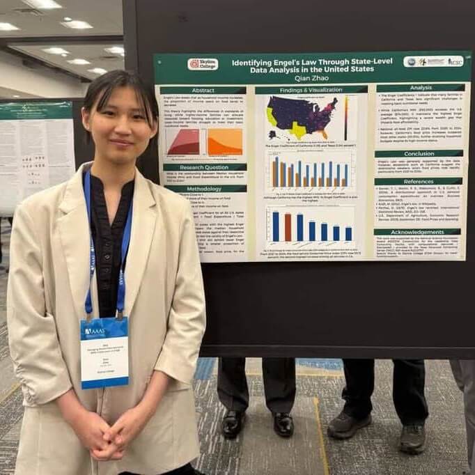 Qian Zhao stands in professional attire in front of her science poster presentation