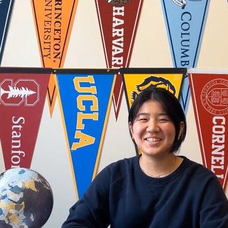 Thiri smiles in front of a wall of university penants in the Transfer Center