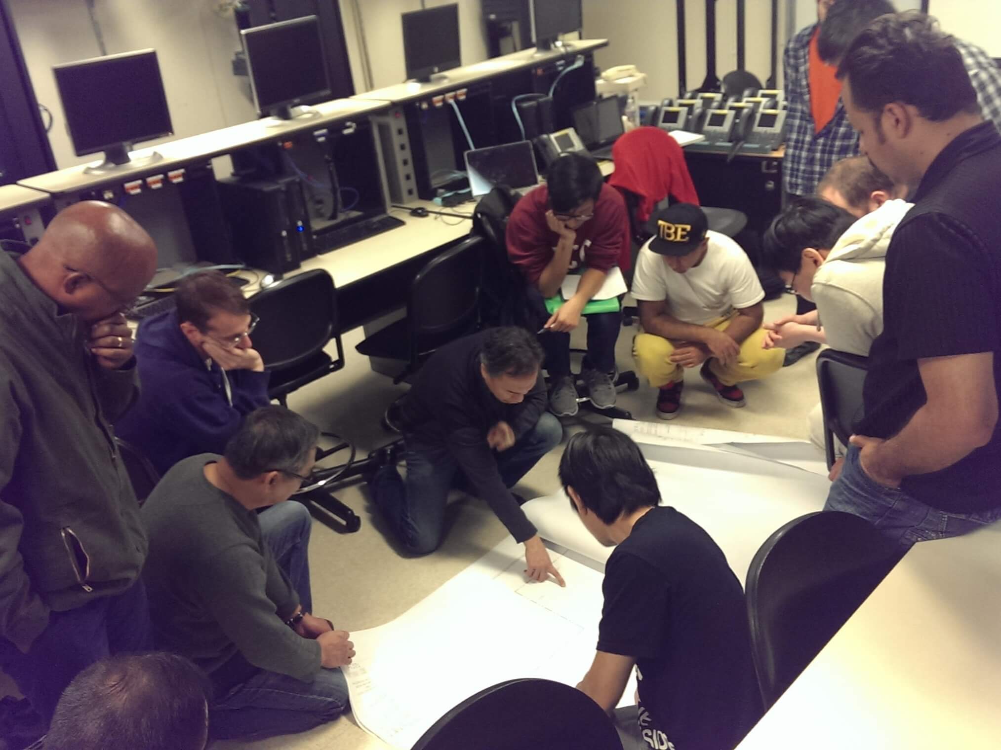 The class gathers around a set of blueprints spread out on the floor