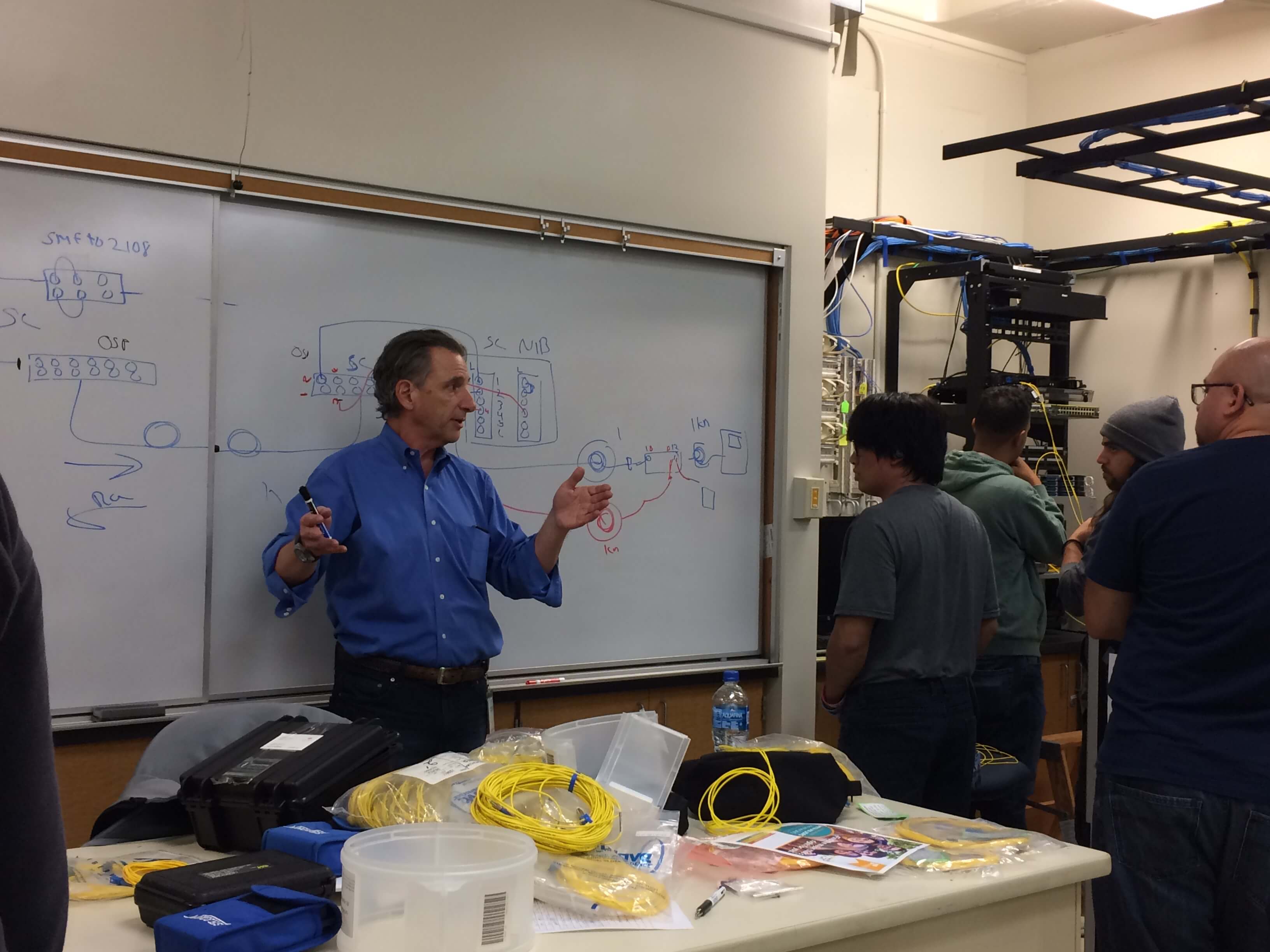 A faculty member stands at the whiteboard and speaks to students