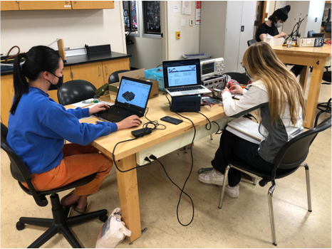 three students working with computers and technology in physics lab