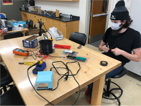 One student working with pliers and wires on a device in physics lab