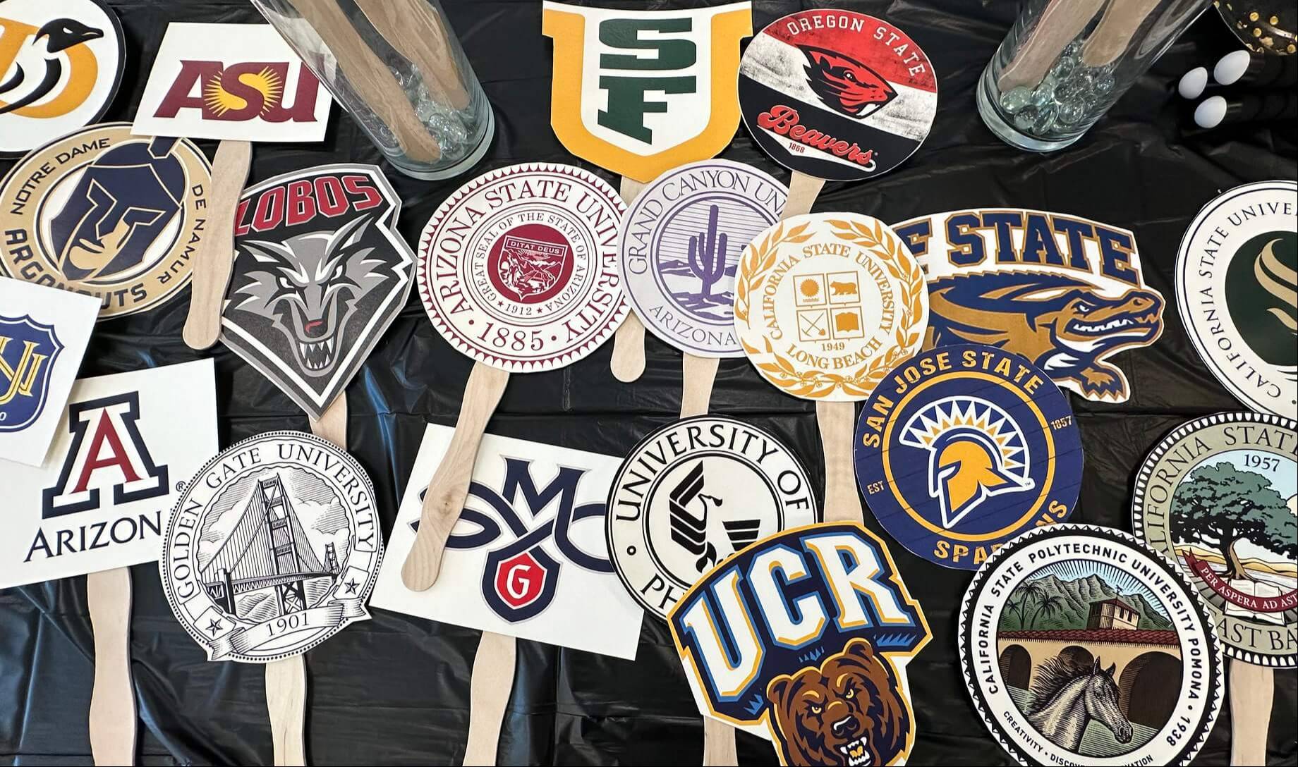 hold-up signs with various college logos lay scattered against a black tablecloth